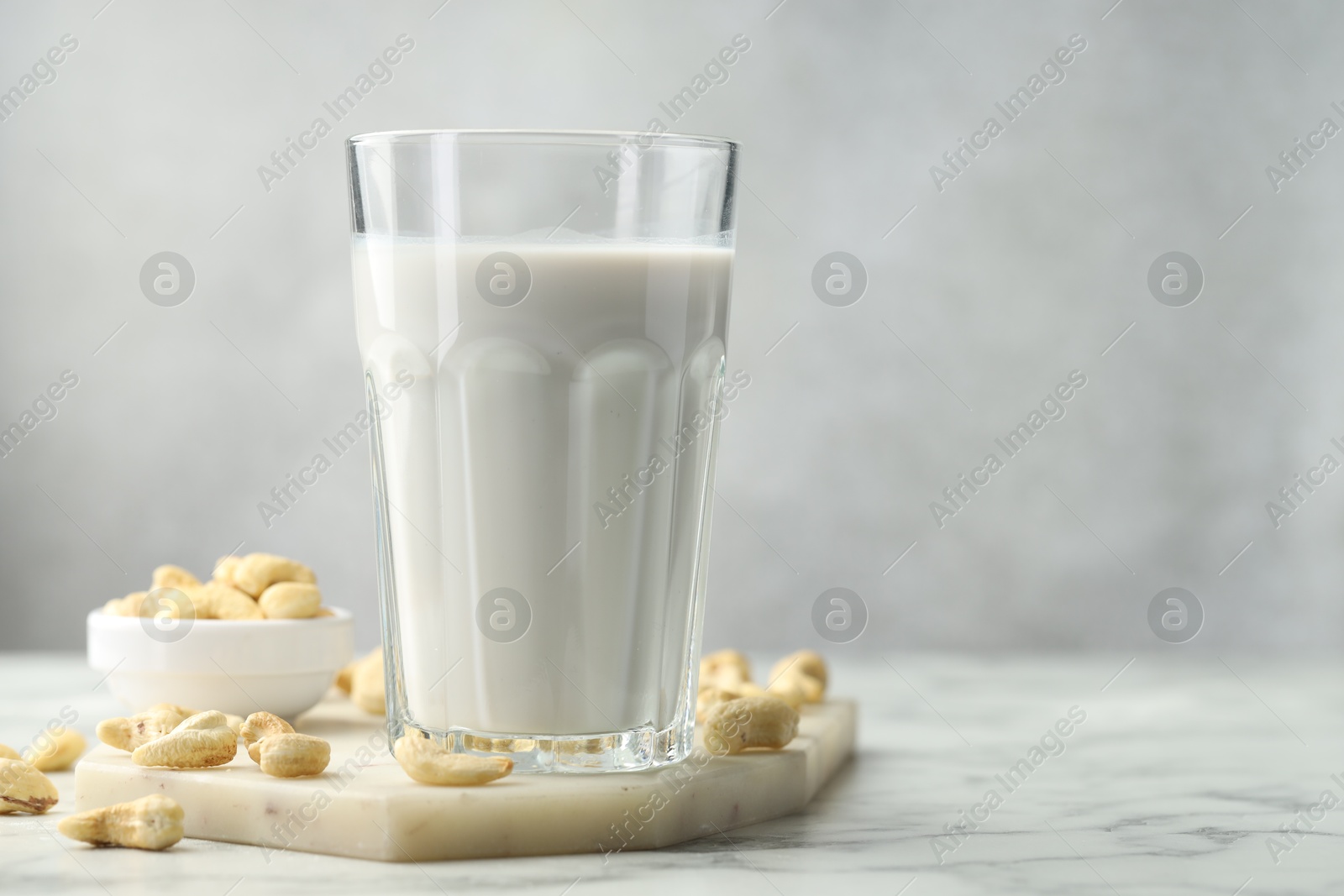 Photo of Fresh cashew milk in glass and nuts on white marble table against light background, closeup. Space for text