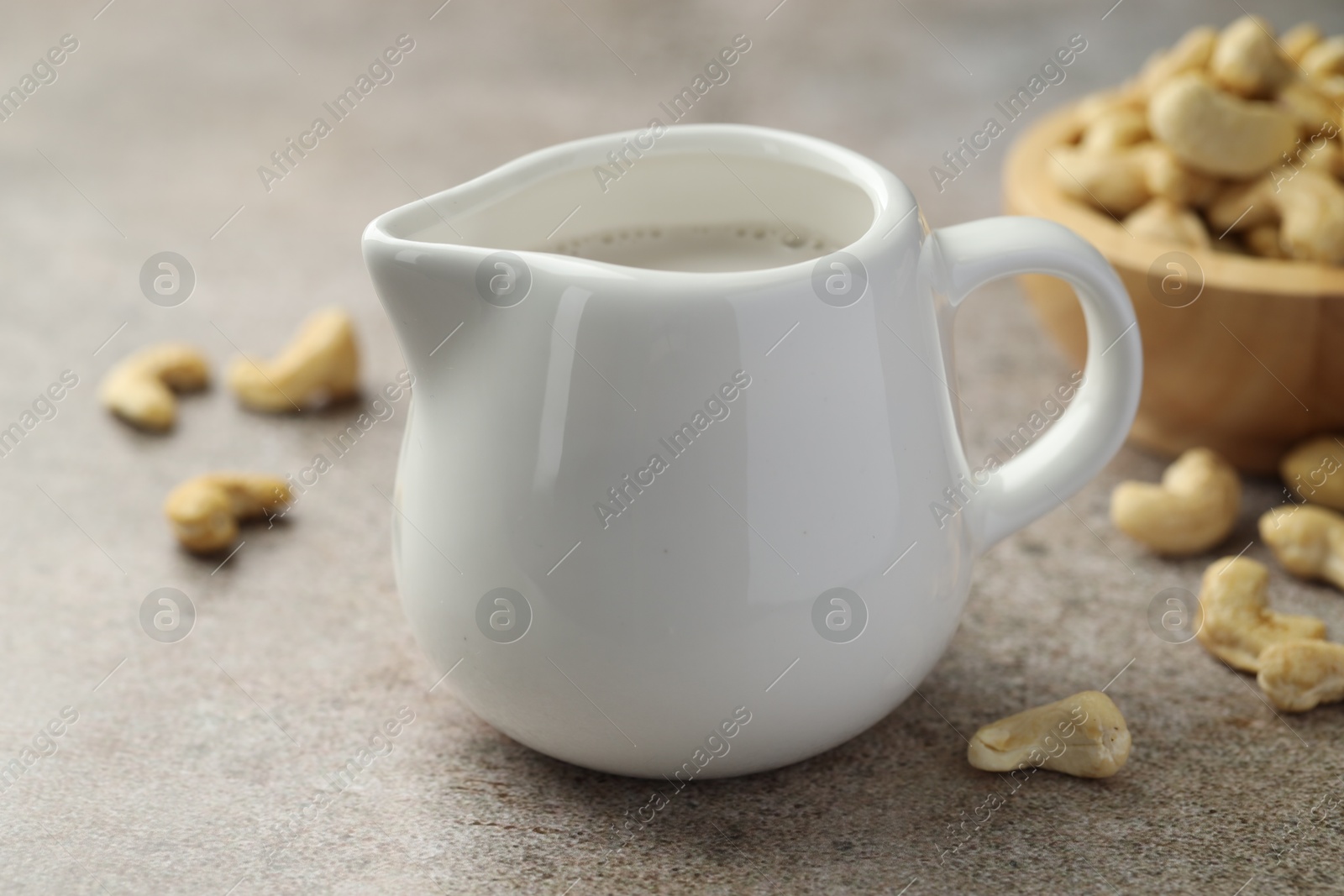 Photo of Fresh cashew milk and nuts on grey textured table, closeup