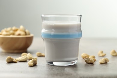 Photo of Fresh cashew milk in glass and nuts on grey textured table, closeup