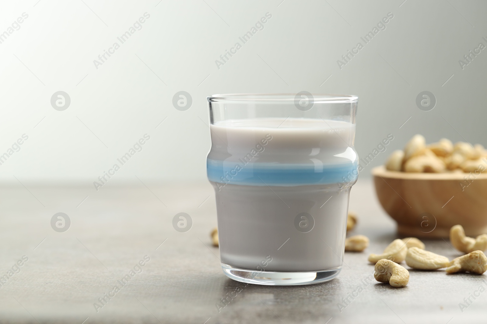 Photo of Fresh cashew milk in glass and nuts on grey table, closeup. Space for text