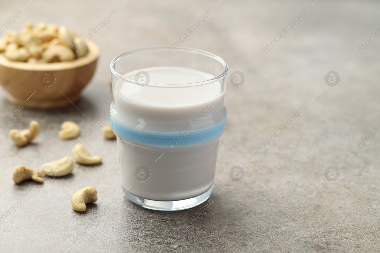 Photo of Fresh cashew milk in glass and nuts on grey textured table, closeup. Space for text