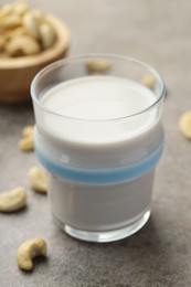 Photo of Fresh cashew milk in glass and nuts on grey textured table, closeup