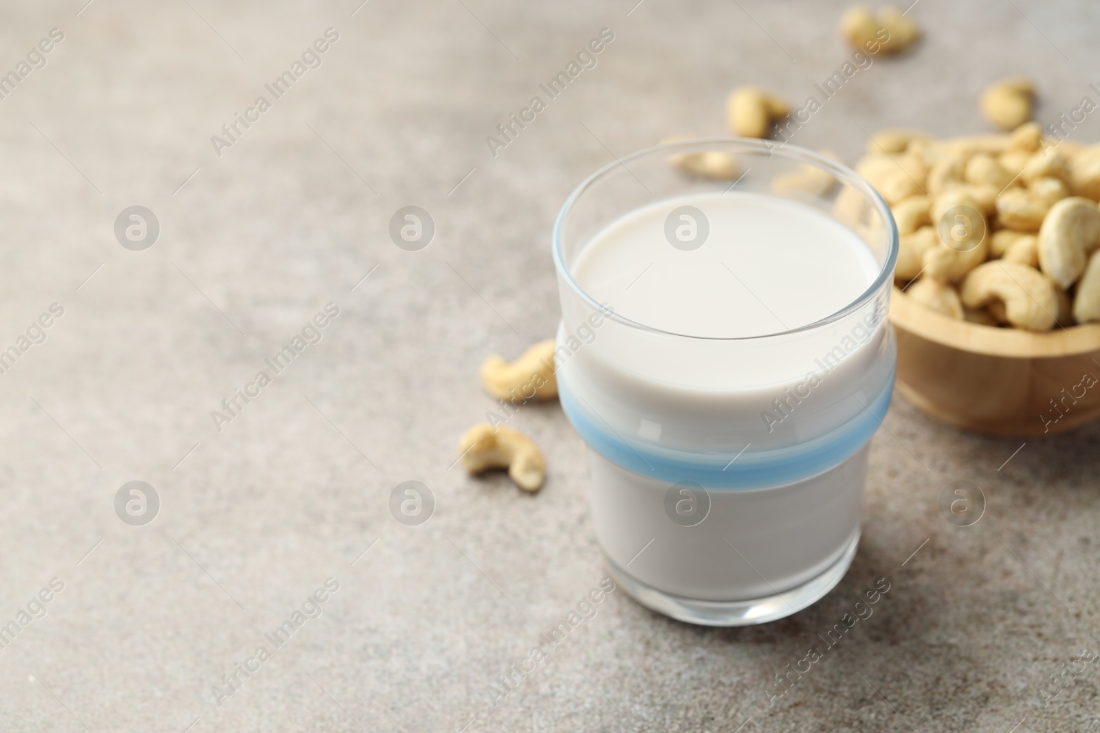 Photo of Fresh cashew milk in glass and nuts on grey textured table, closeup. Space for text