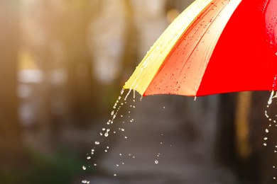 Photo of Open bright umbrella under pouring rain outdoors, closeup