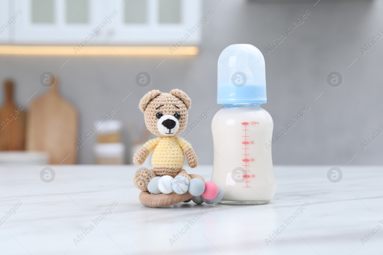 Photo of Feeding bottle with milk, teddy bear and teether on white table indoors