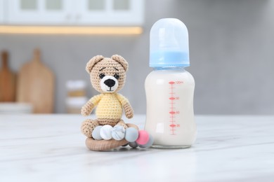 Photo of Feeding bottle with milk, teddy bear and teether on white table indoors