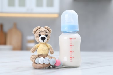 Photo of Feeding bottle with milk, teddy bear and teether on white table indoors