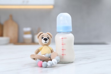 Feeding bottle with milk, teddy bear and teether on white table indoors