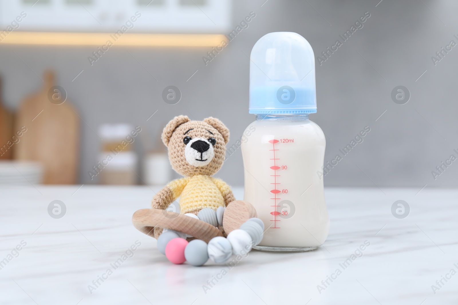 Photo of Feeding bottle with milk, teddy bear and teether on white table indoors