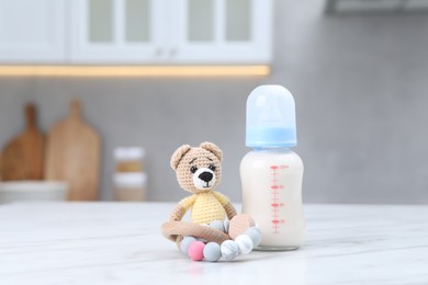 Photo of Feeding bottle with milk, teddy bear and teether on white table indoors. Space for text