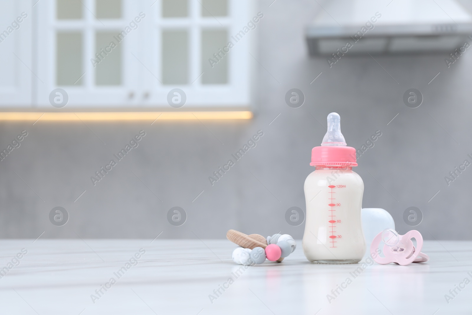 Photo of Feeding bottle with milk, pacifier and teether on white table indoors. Space for text