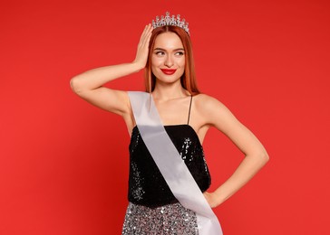 Photo of Beautiful young woman with tiara and ribbon in dress on red background