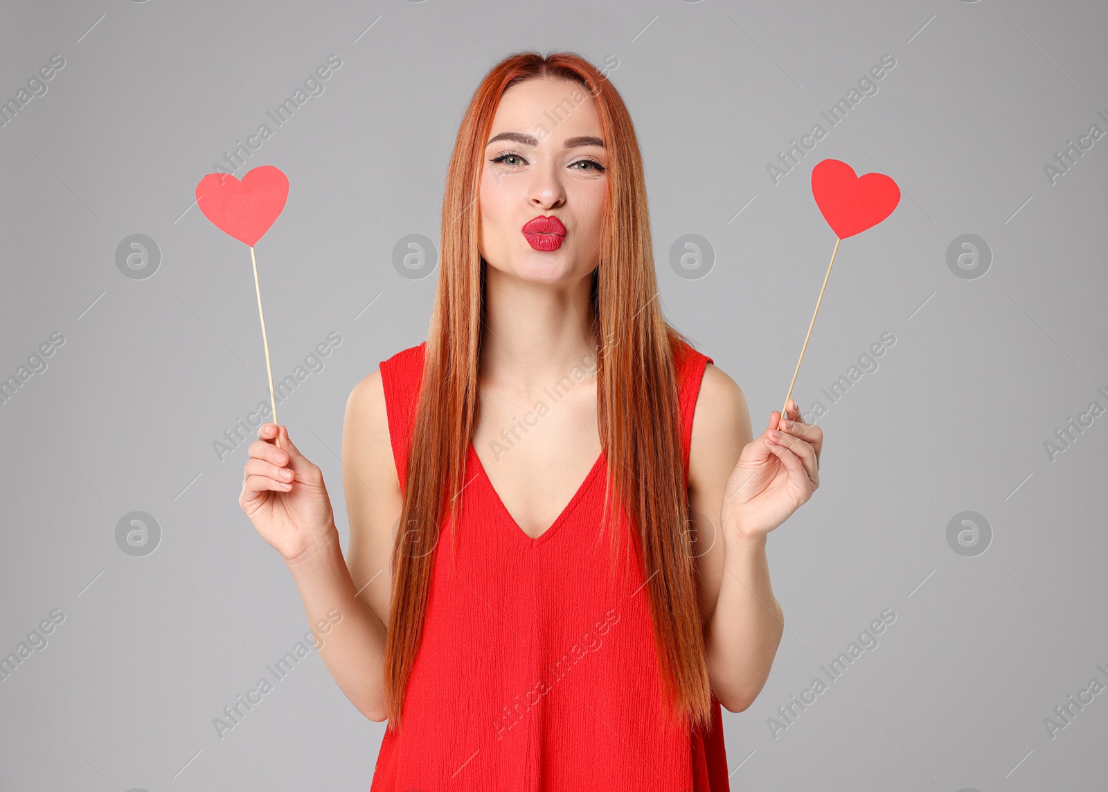 Photo of Young woman in red dress with paper hearts on light grey background