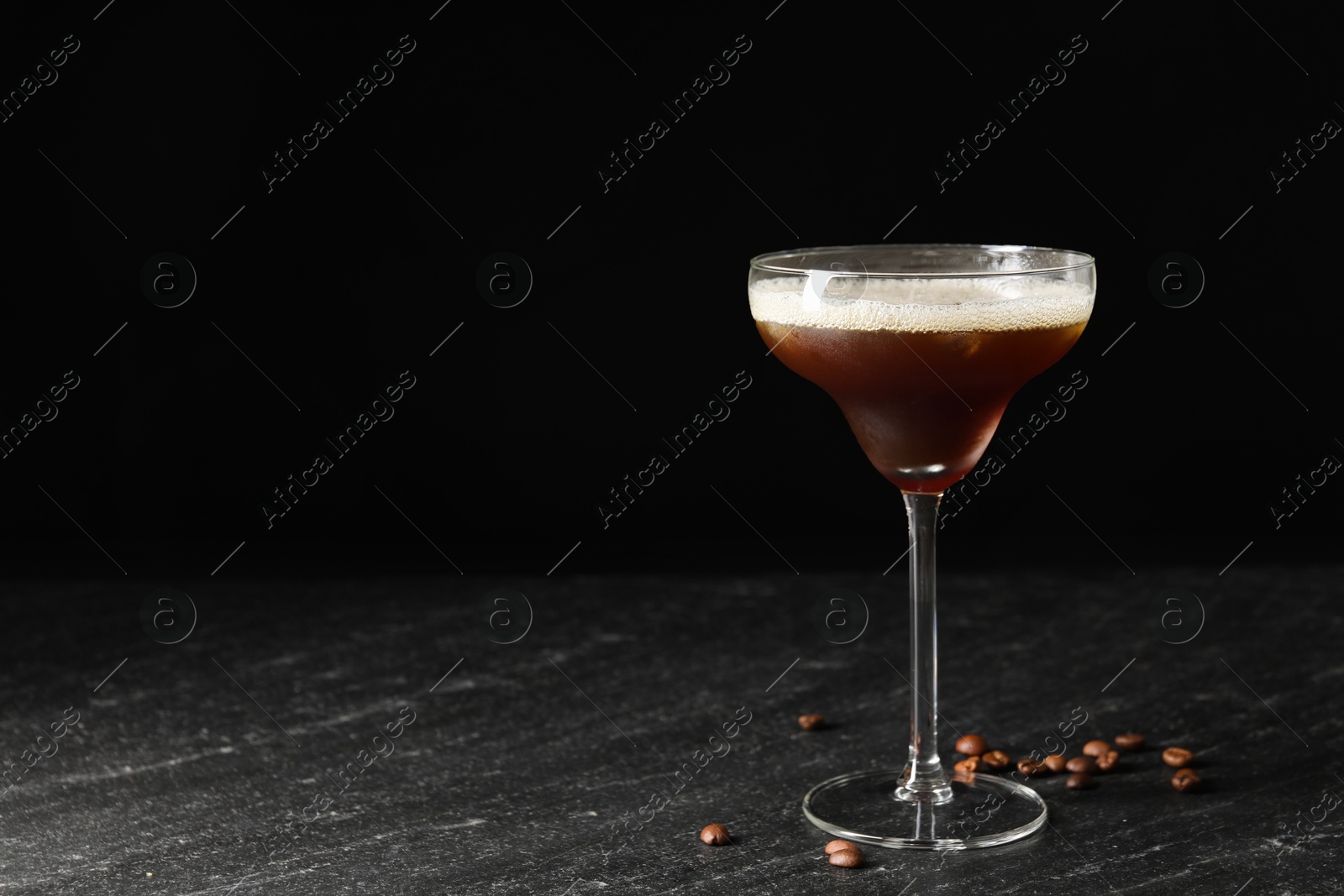 Photo of Glass of delicious espresso martini and coffee beans on dark textured table. Space for text