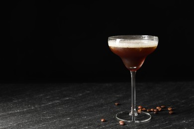 Photo of Glass of delicious espresso martini and coffee beans on dark textured table. Space for text