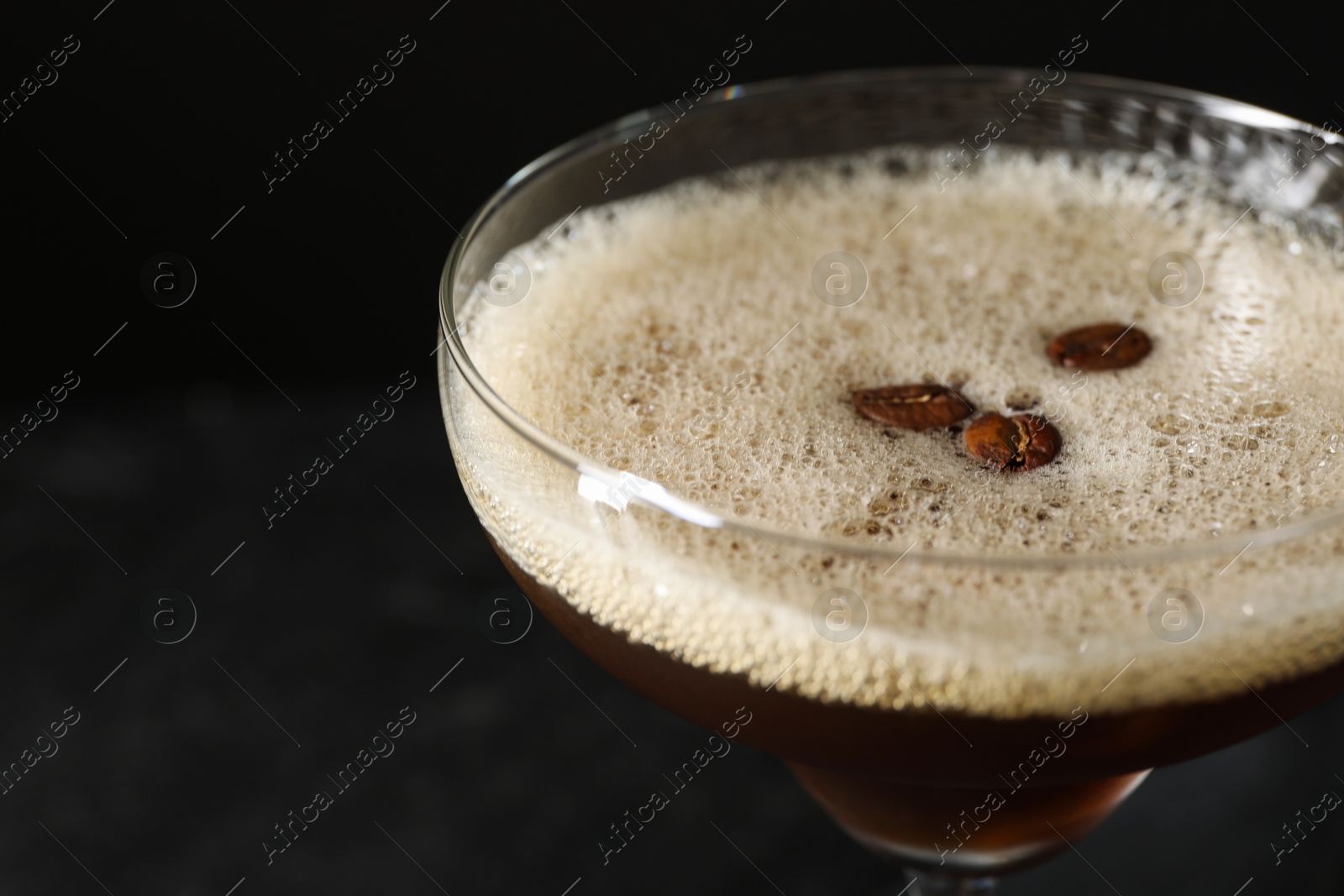 Photo of Delicious espresso martini with coffee beans in glass on black background, closeup