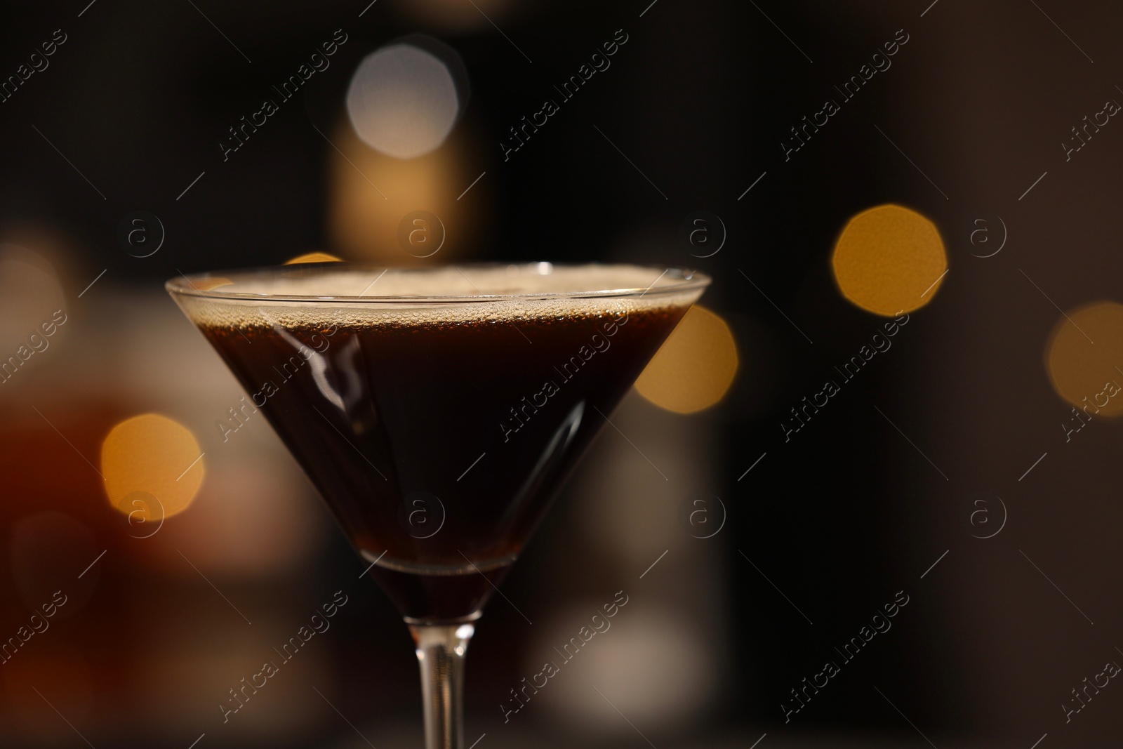 Photo of Delicious espresso martini in glass against blurred lights, closeup