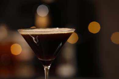 Photo of Delicious espresso martini in glass against blurred lights, closeup