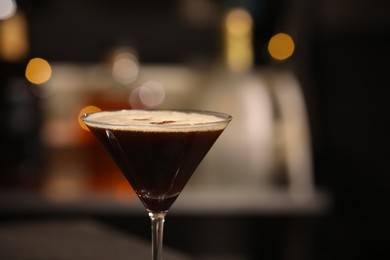 Photo of Delicious espresso martini in glass against blurred lights, closeup