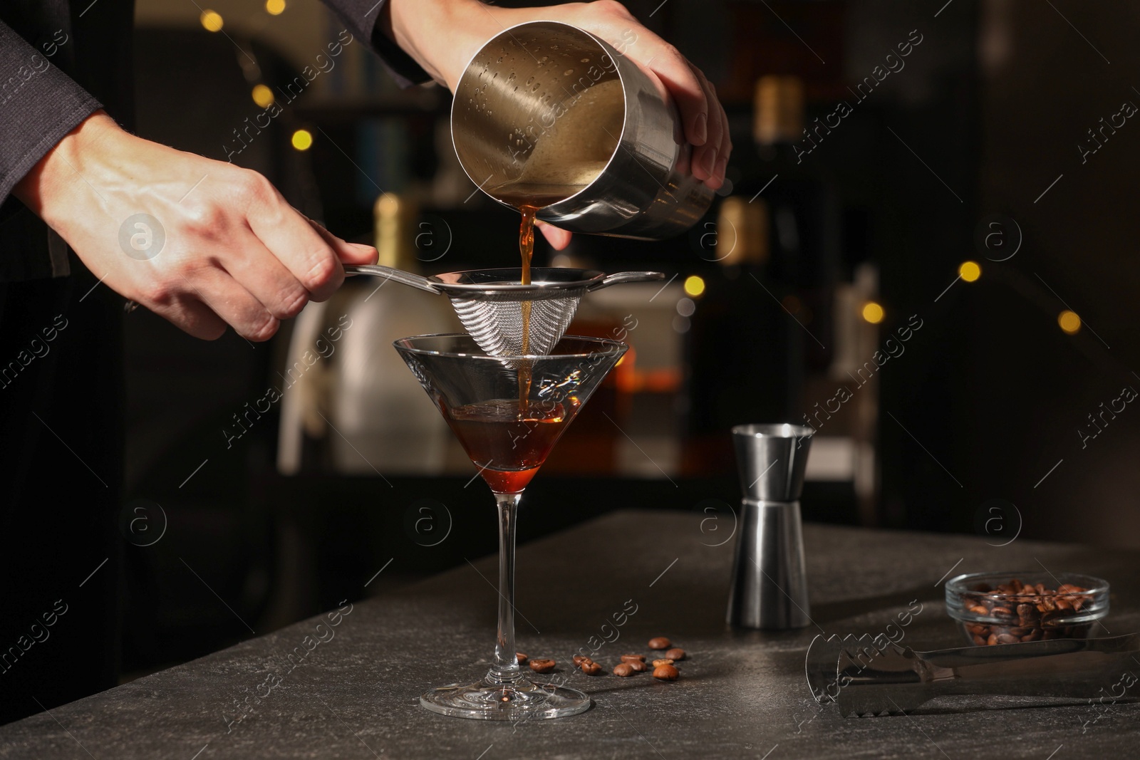 Photo of Bartender making delicious espresso martini at dark table against blurred lights, closeup