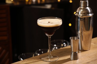 Photo of Glass with delicious espresso martini, jigger and shaker on wooden table in bar