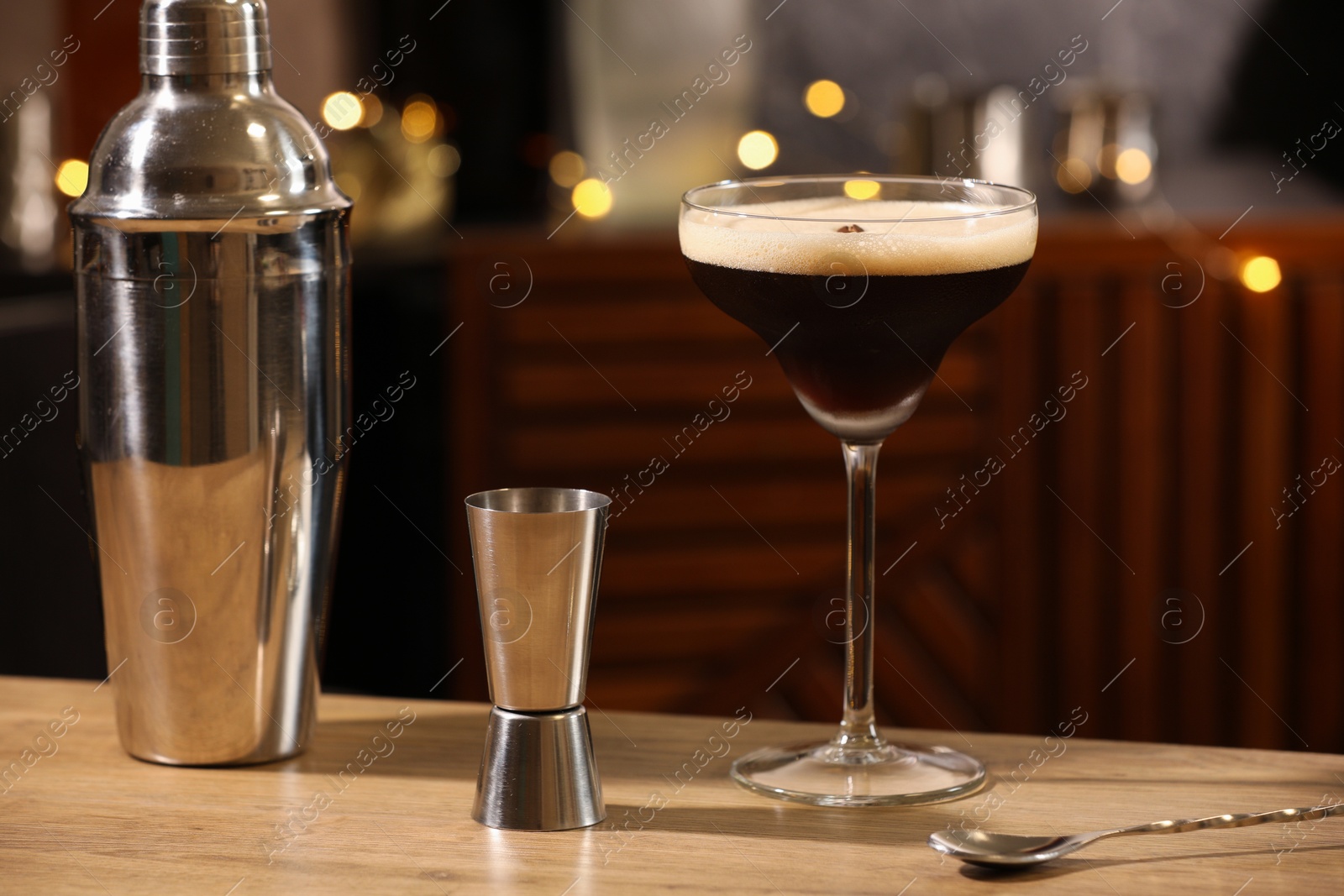 Photo of Glass with delicious espresso martini, jigger and shaker on wooden table in bar