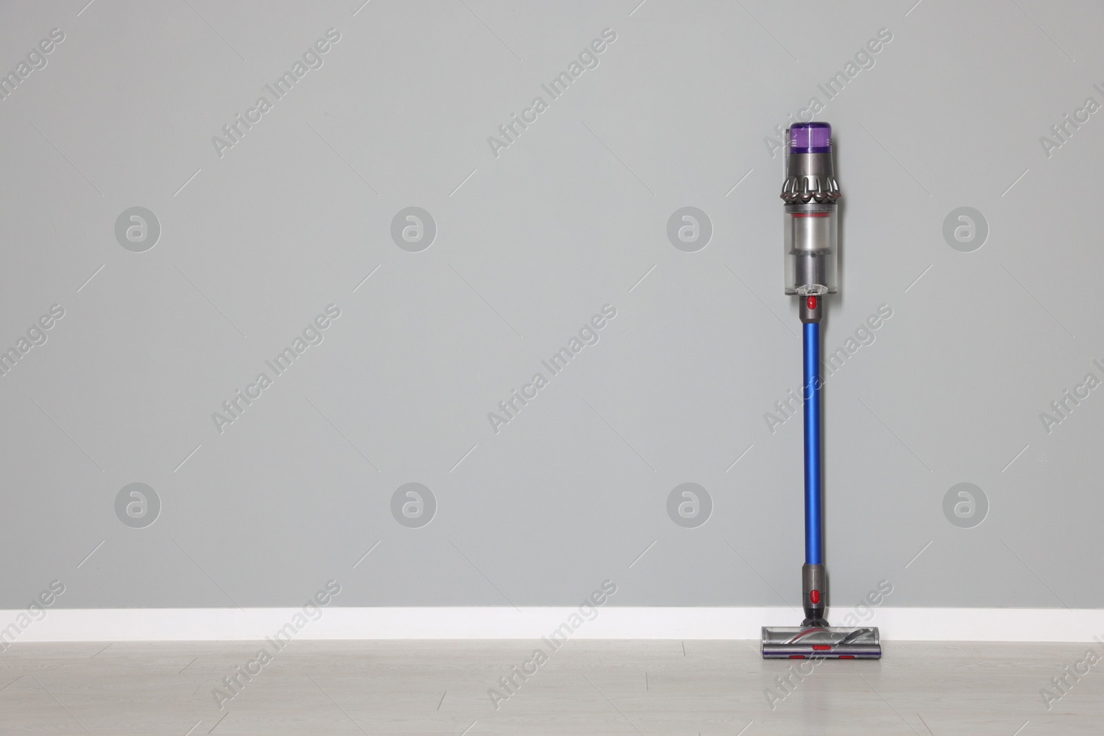 Photo of One cordless vacuum cleaner near grey wall indoors. Space for text