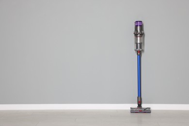 Photo of One cordless vacuum cleaner near grey wall indoors. Space for text