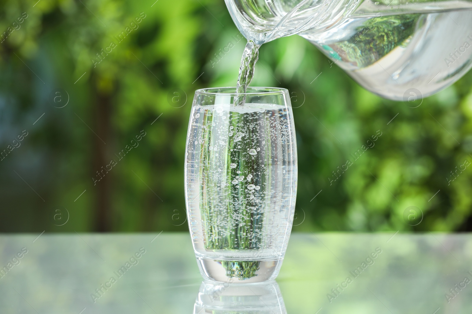 Photo of Pouring soda water in glass at light table outdoors