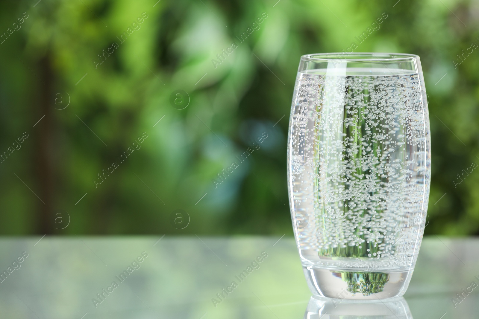 Photo of Soda water in glass on light table outdoors, space for text