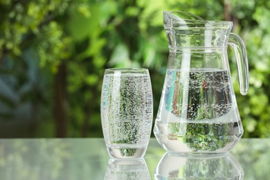 Photo of Soda water in glass and jug on light table outdoors