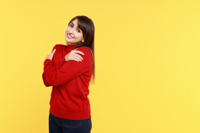 Photo of Young woman hugging himself on yellow background, space for text