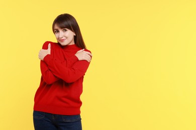 Photo of Young woman hugging himself on yellow background, space for text