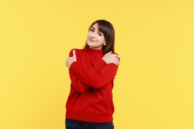 Photo of Young woman hugging himself on yellow background