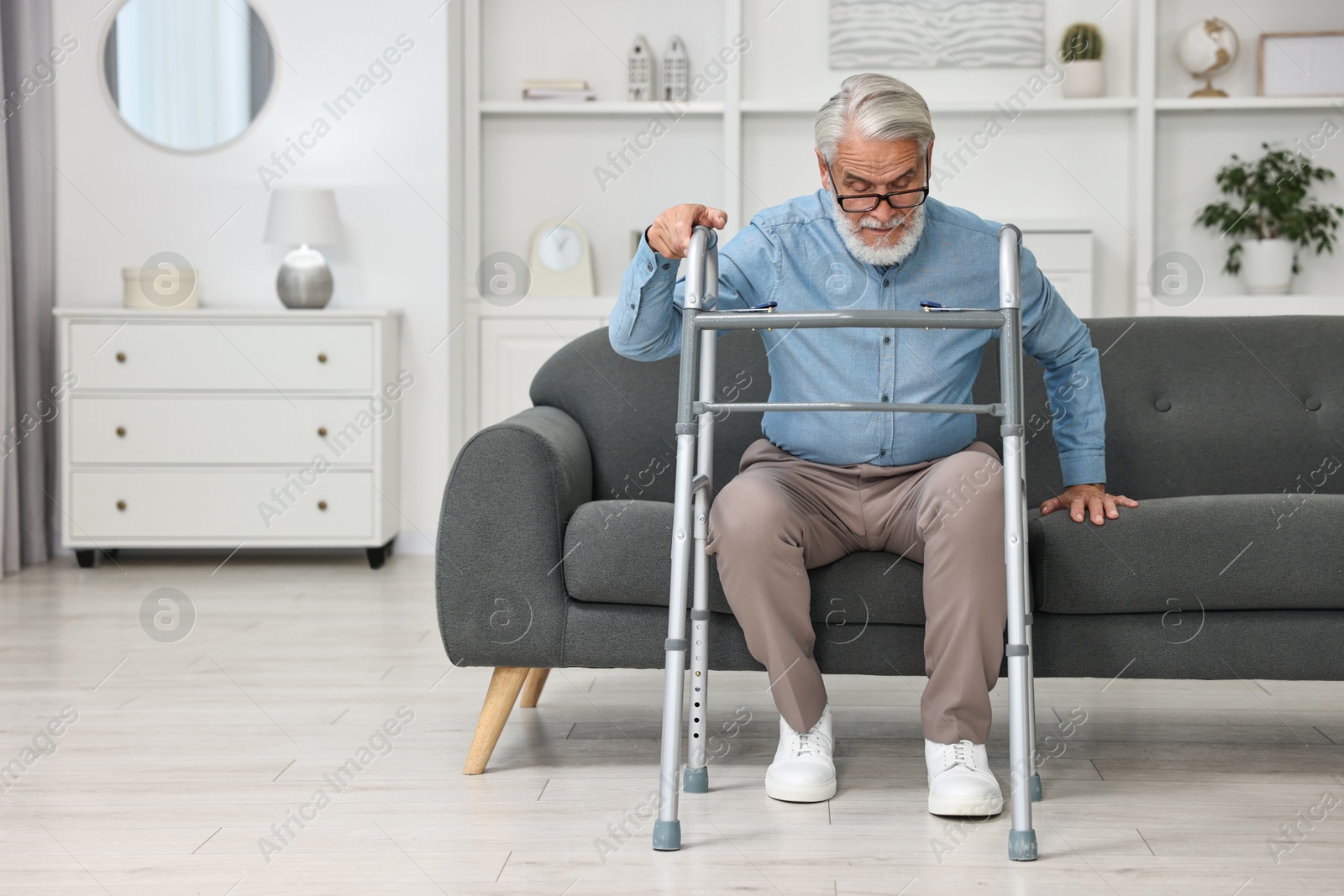 Photo of Senior man with walking frame on sofa at home