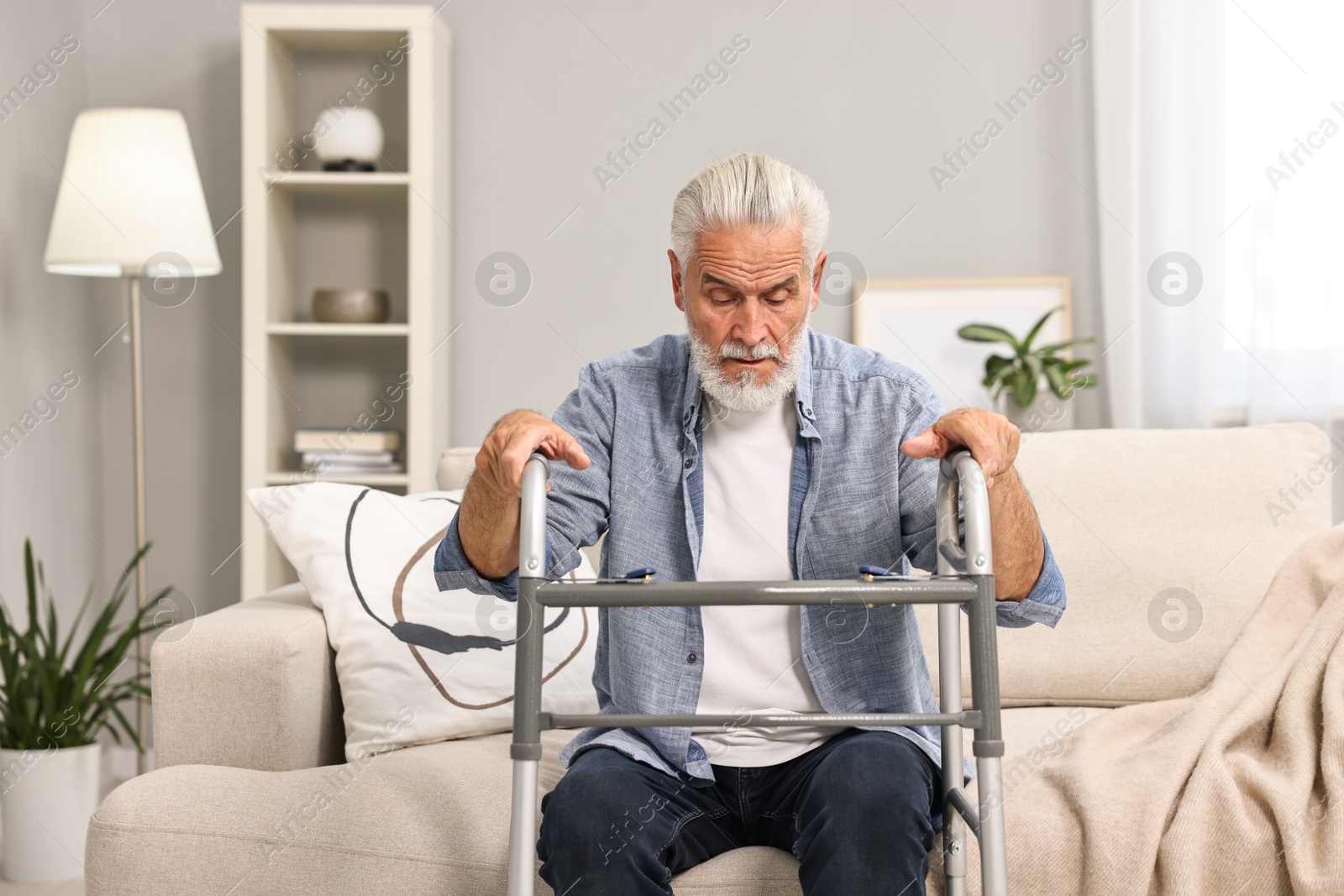 Photo of Senior man with walking frame on sofa at home