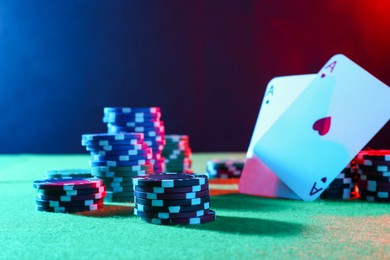 Photo of Poker chips and playing cards on green table in neon lights, closeup