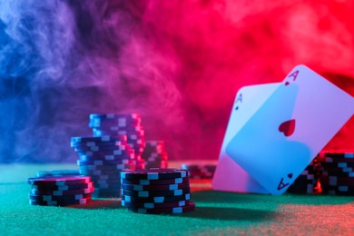 Poker chips and playing cards on green table in neon lights, closeup