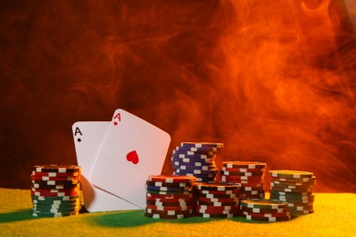 Photo of Poker chips and playing cards on green table in neon lights