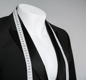 Photo of Male mannequin with elegant suit jacket and measuring tape on grey background, closeup