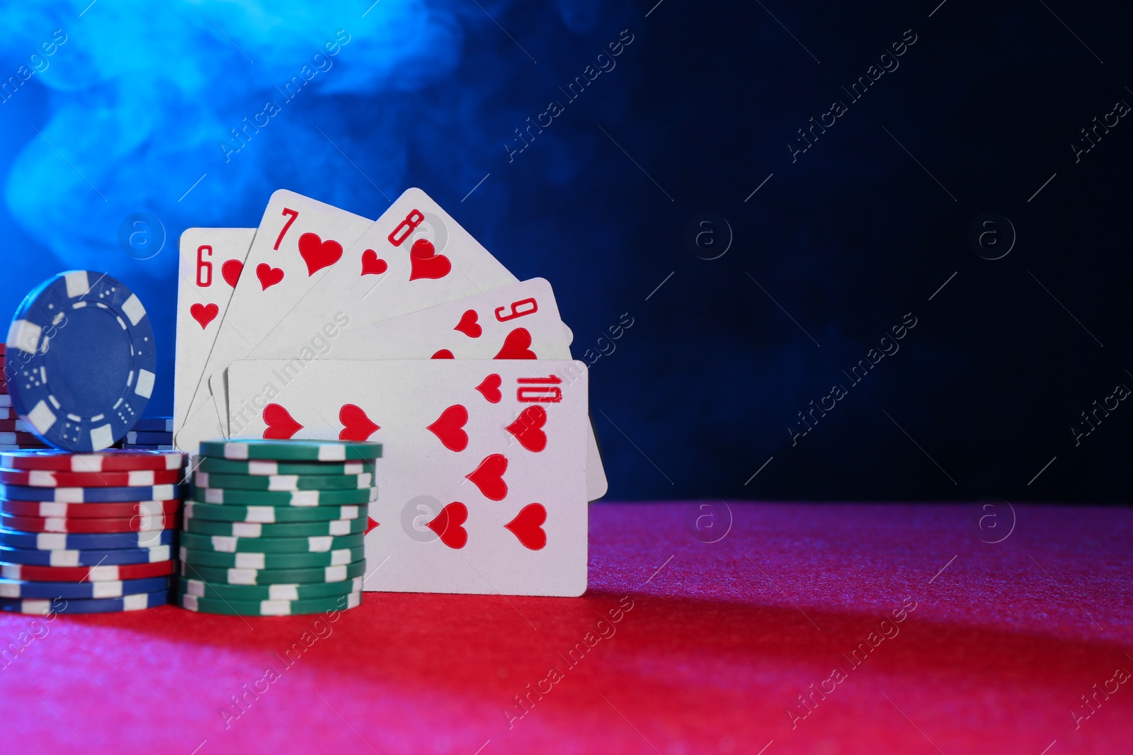 Photo of Poker chips and playing cards on pink table in neon lights, space for text