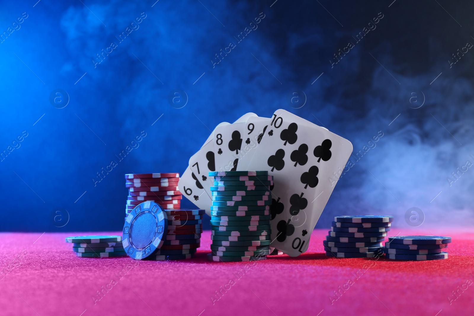 Photo of Poker chips and playing cards on pink table