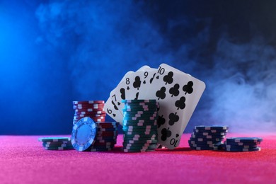 Photo of Poker chips and playing cards on pink table