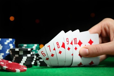 Photo of Poker game. Woman with playing cards and chips at green table, closeup