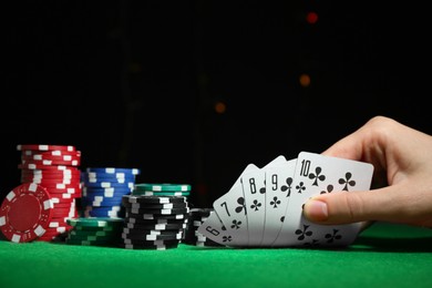 Photo of Poker game. Woman with playing cards and chips at green table, closeup