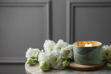 Burning candle and beautiful flowers on marble table. Space for text