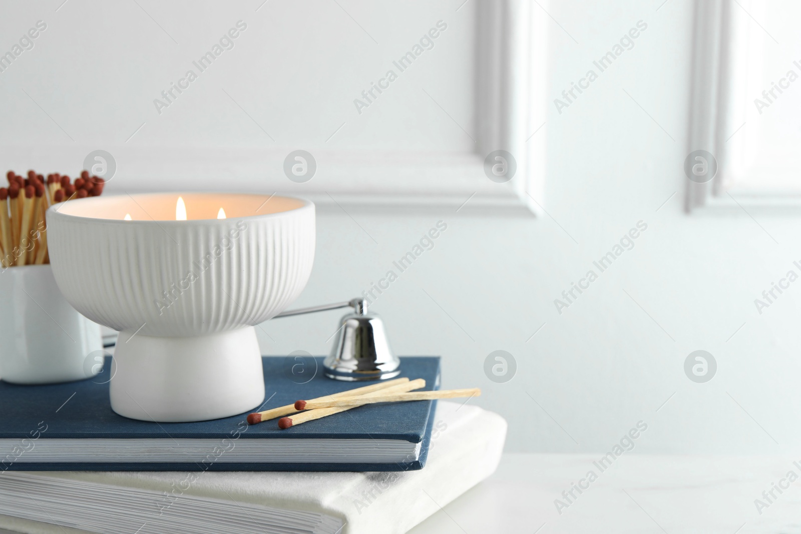 Photo of Burning candle, matches, books and bell on white marble table, closeup. Space for text