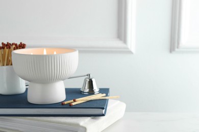 Photo of Burning candle, matches, books and bell on white marble table, closeup. Space for text