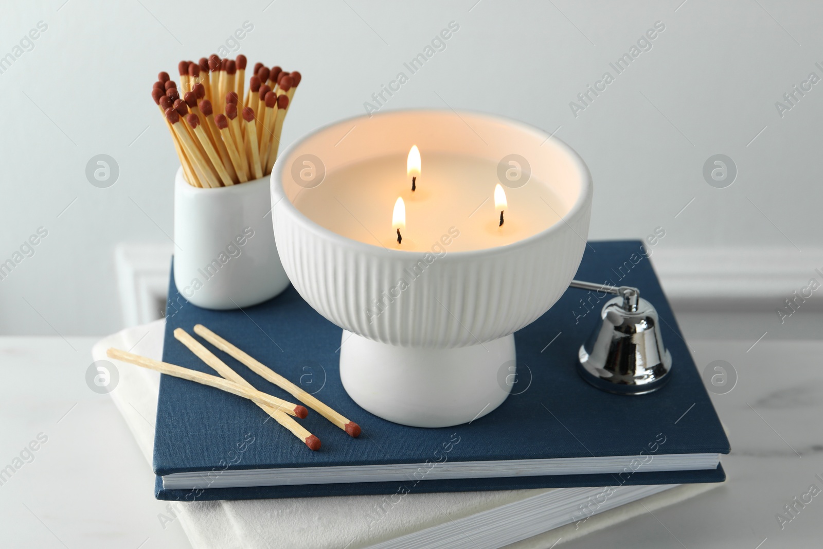 Photo of Burning candle, matches, books and bell on white marble table, closeup