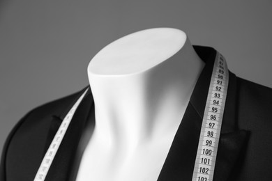 Photo of Mannequin with black jacket and measuring tape on grey background, closeup